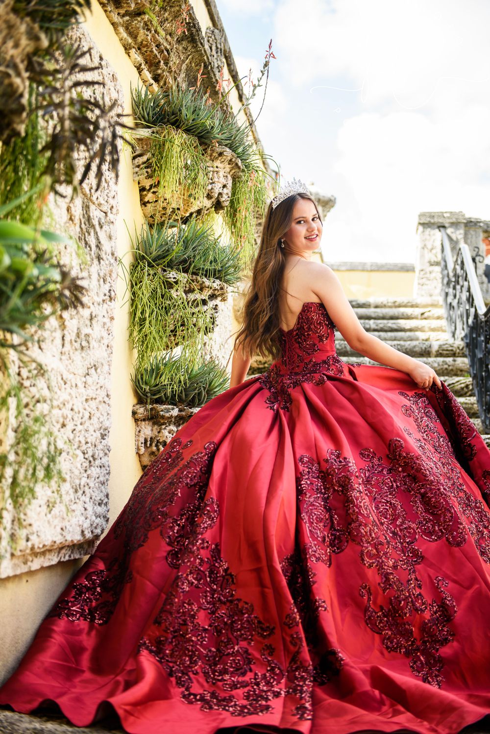 A stunning red ball gown with black lace details photographed against stone walls and steps in an outdoor setting.