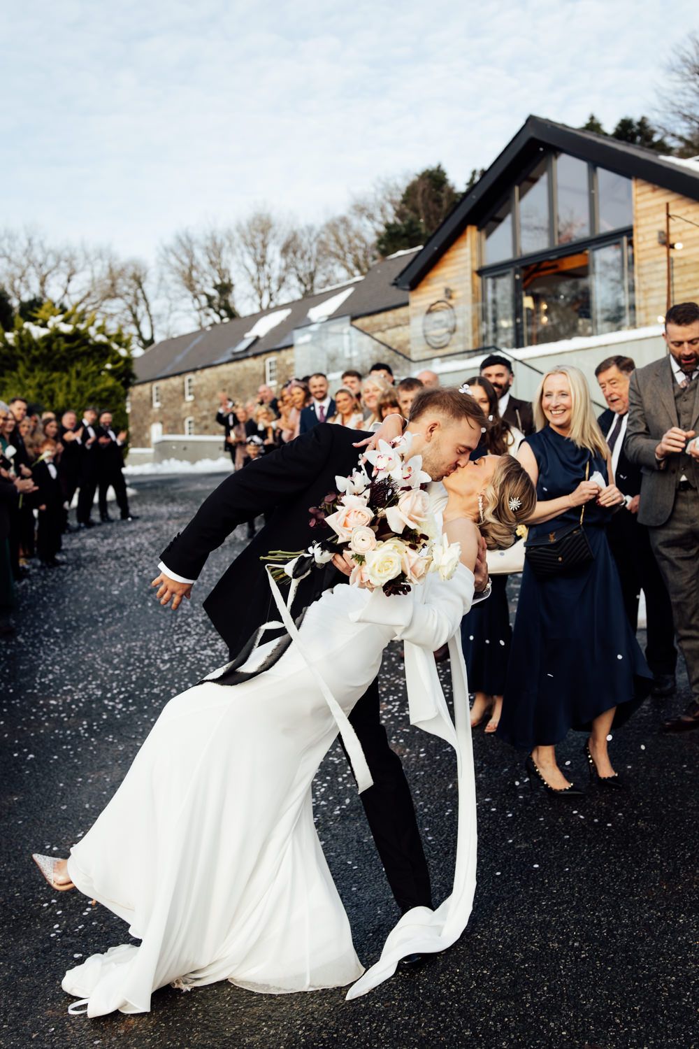 Wedding party poses playfully with bride and groom in dramatic dip poses following their confetti moment at Gellifawr.