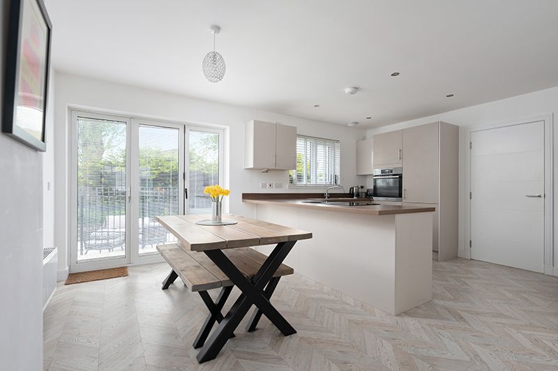 Modern open concept living space with white walls, natural light, and black X-frame dining table in a minimalist setting.