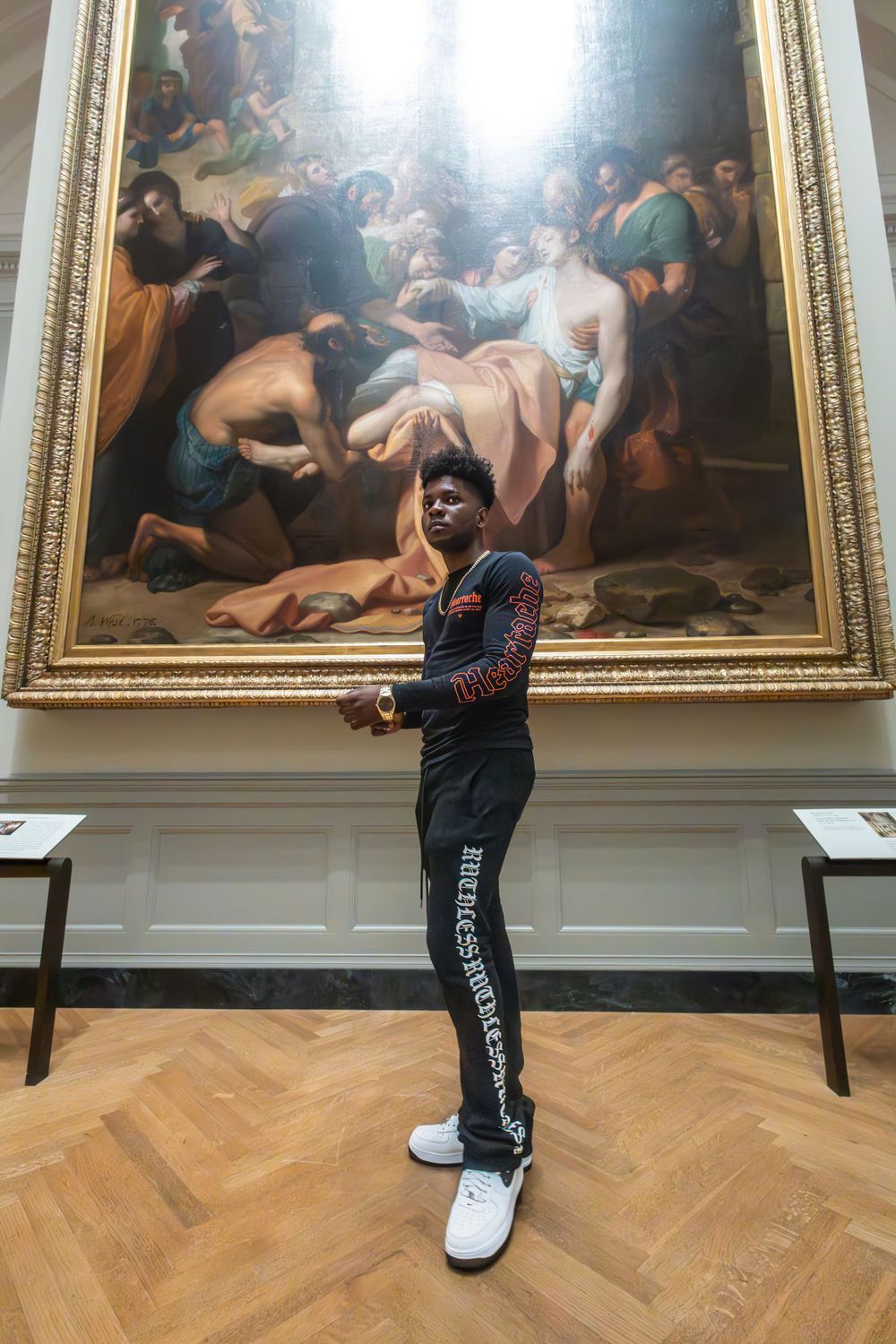 A museum visitor admiring a large classical painting in an ornate gold frame.