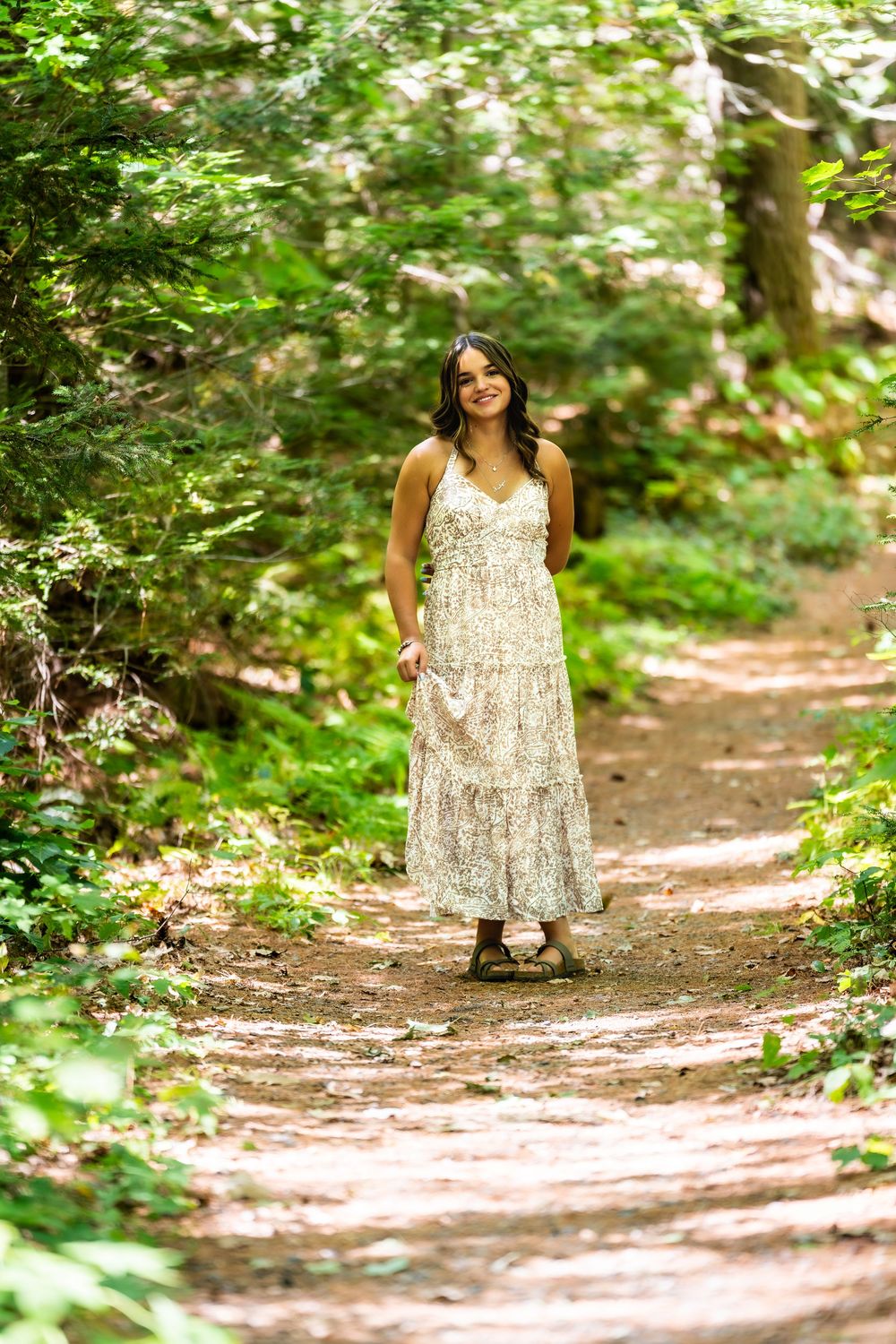 Person in floral dress walking along a sunlit forest path.