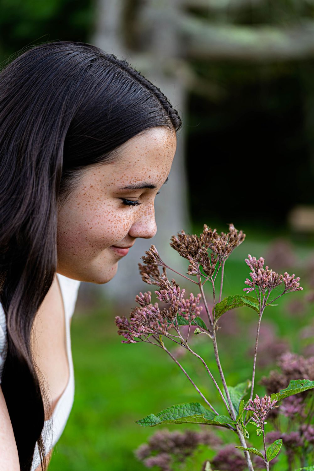 Person leaning forward to smell pink wildflowers in natural outdoor setting.