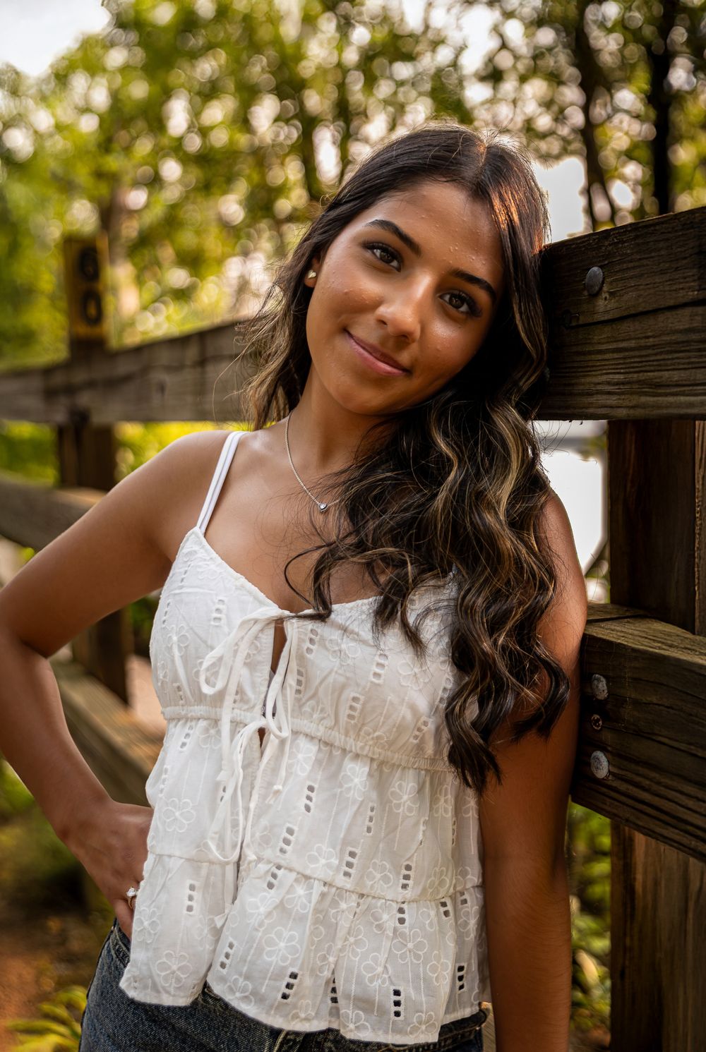 Person wearing white eyelet lace dress poses against wooden fence in natural setting.