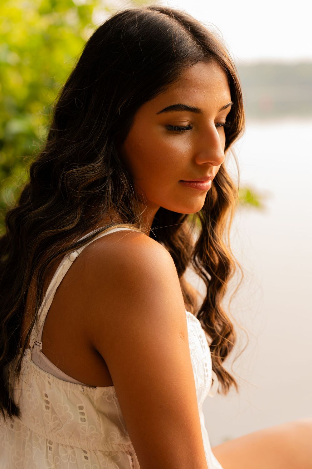 Person in white sleeveless top poses against bright natural background.