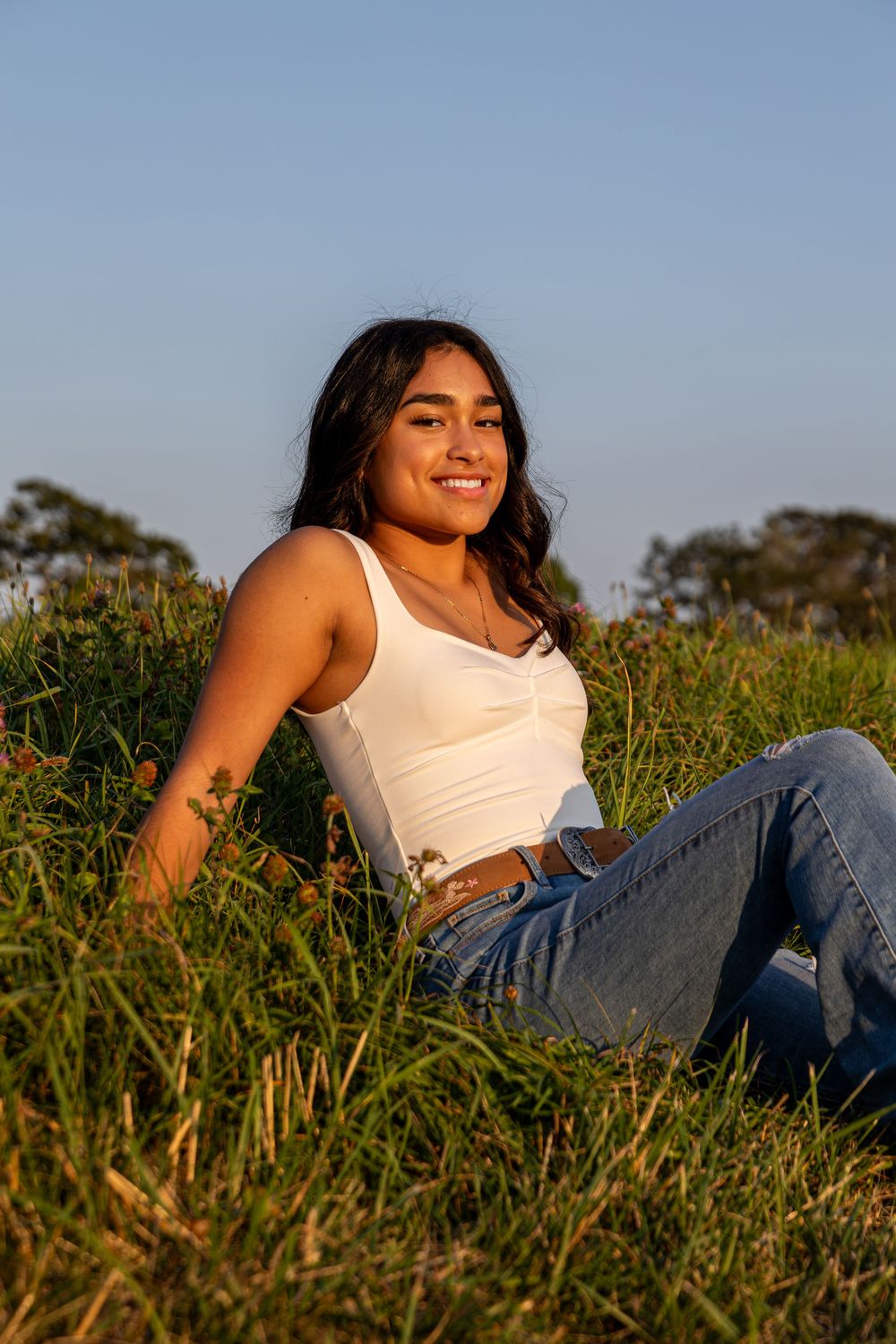 Person relaxing in grass during golden hour wearing casual white tank top and jeans.