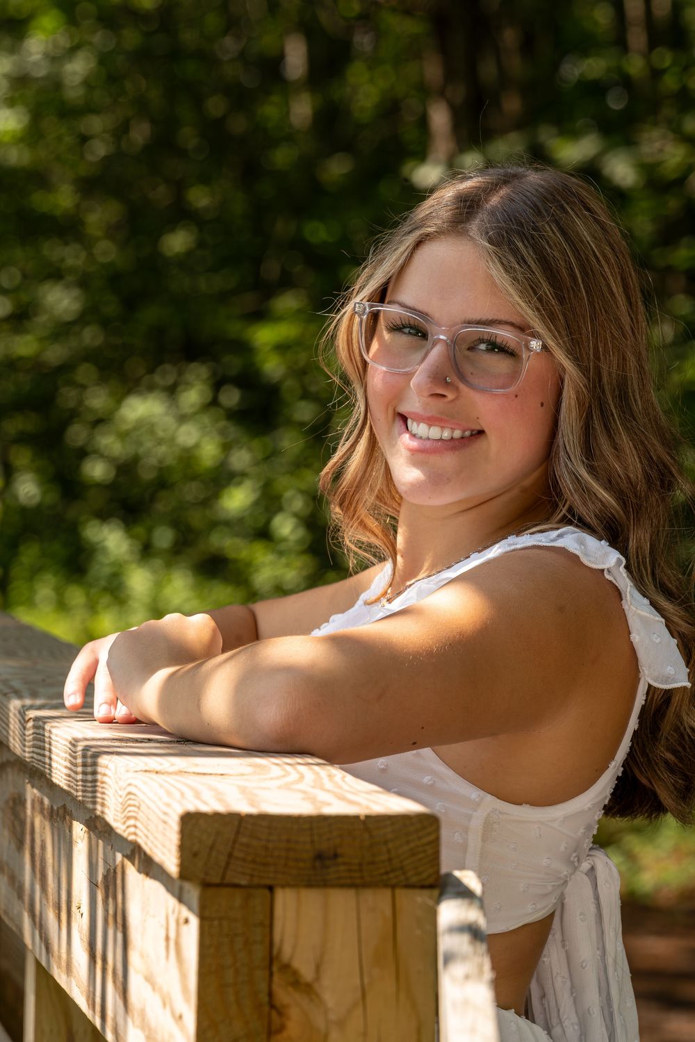 A summer portrait featuring a white sundress and wooden fence in natural lighting.