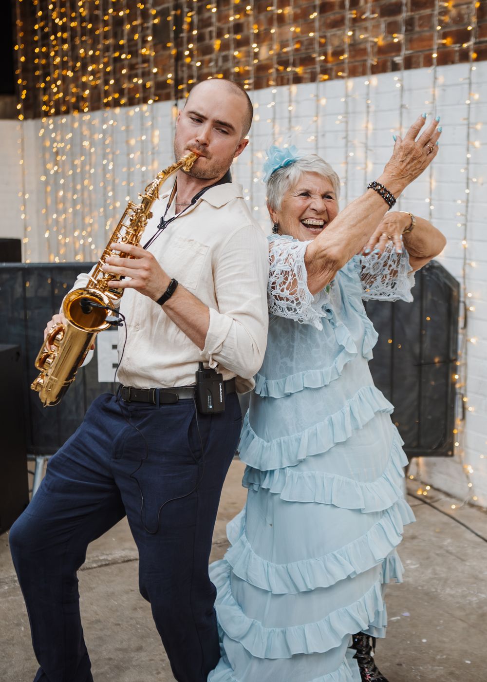 People dancing joyfully under twinkling string lights at a festive event.