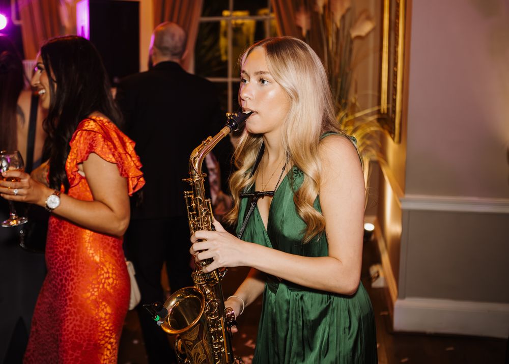 Saxophonist playing at a party where guests dance.