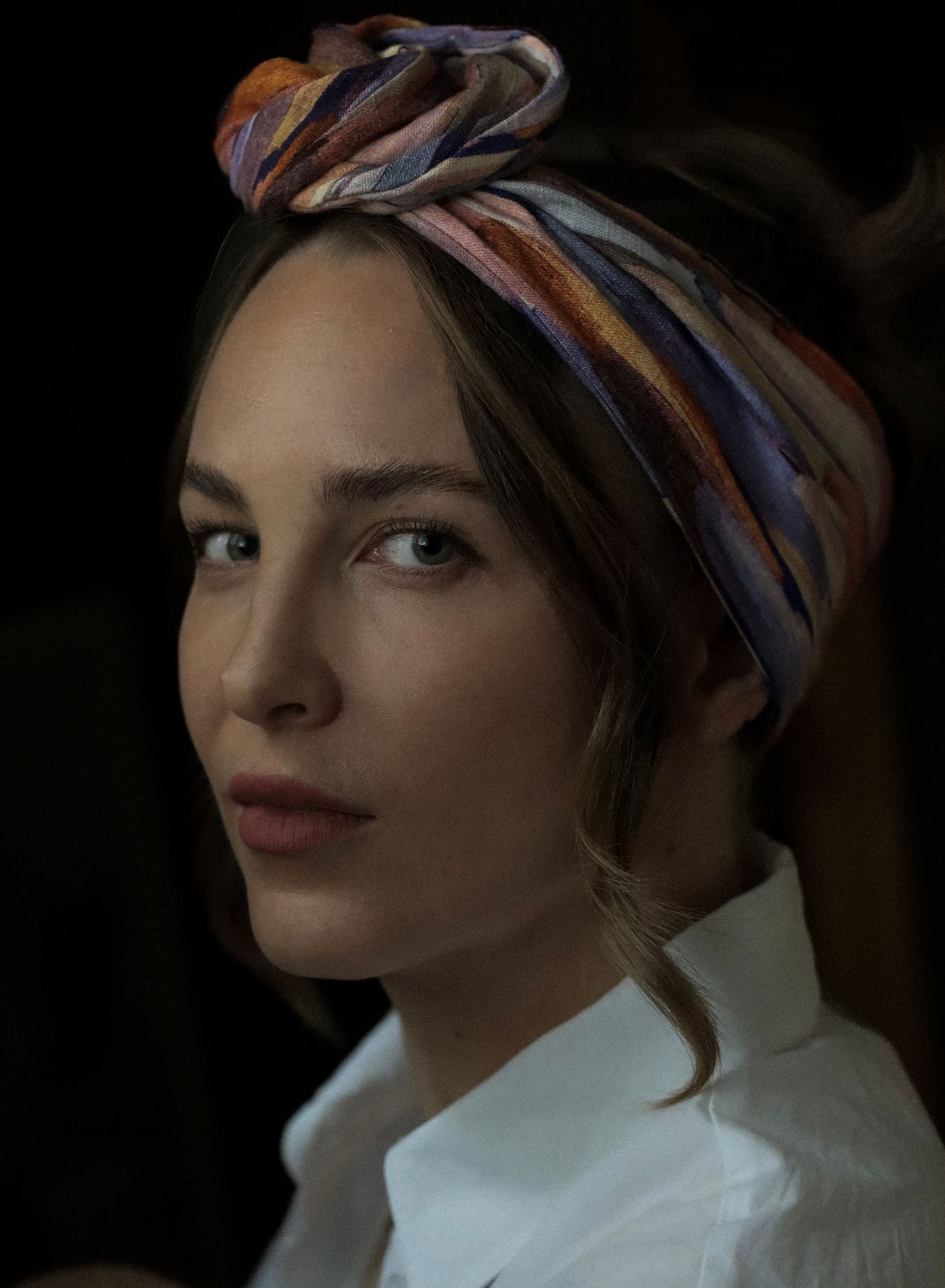 Classic portrait featuring multicolored striped headpiece and white collared shirt against dark background.