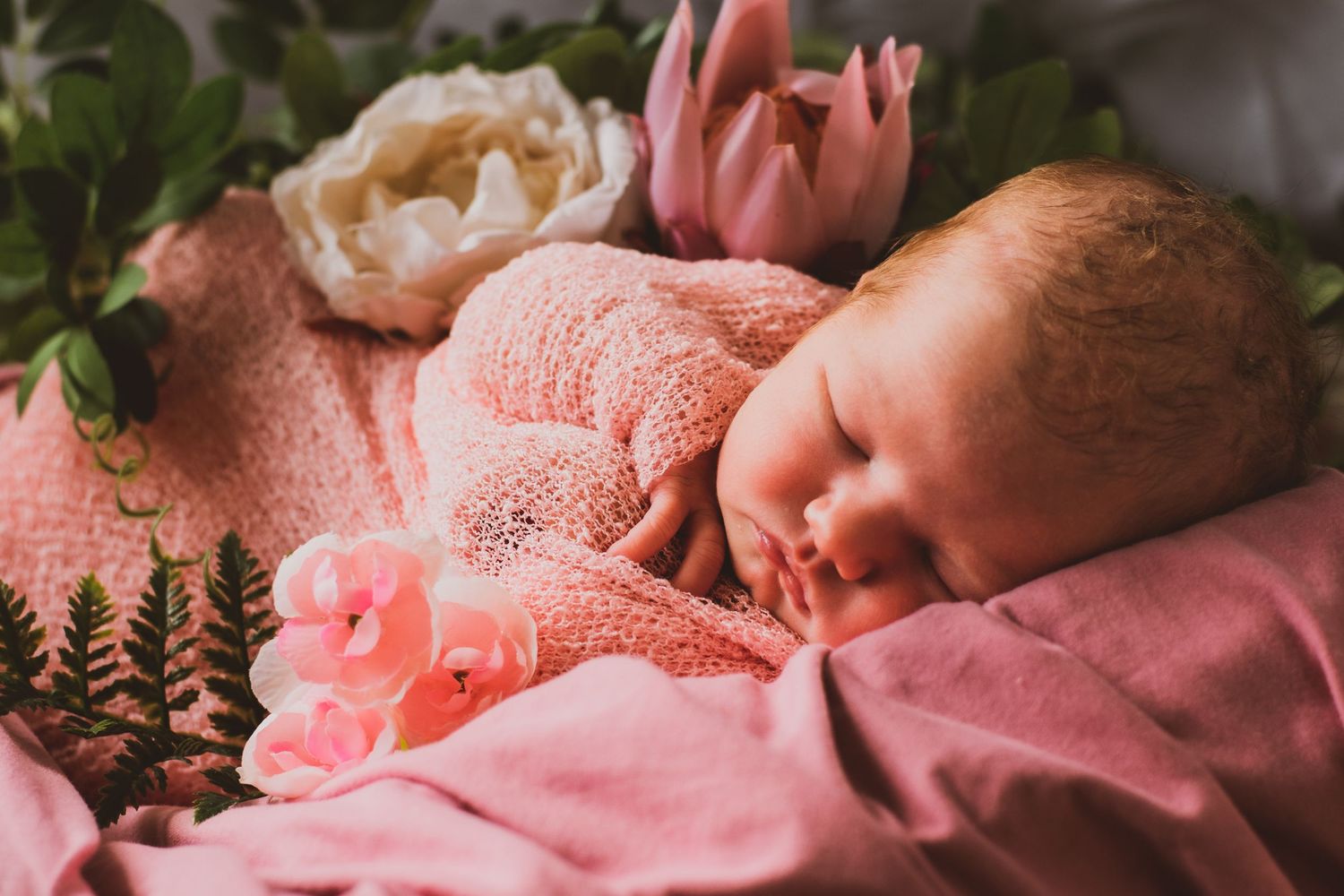Close-up of sleeping newborn with pink blanket and floral decorations.