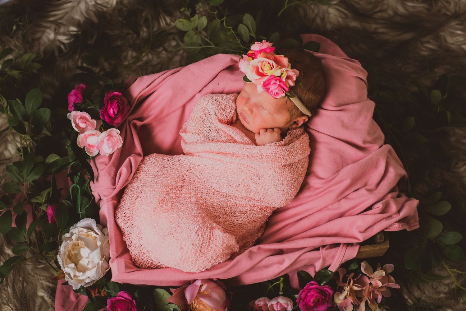Newborn photography with pink wraps and floral decorations in garden setting.