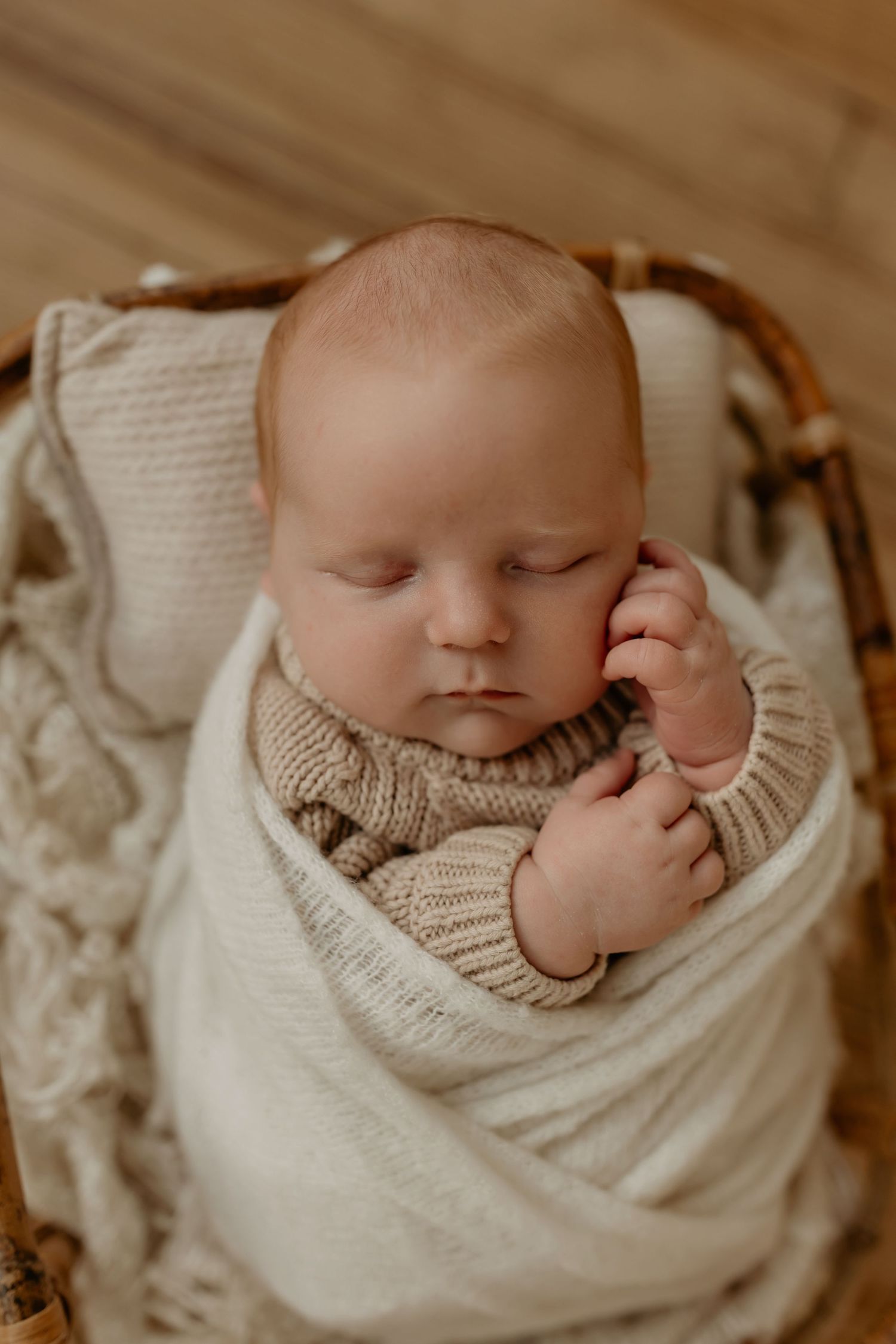 Sleeping infant wearing knitted cream romper with floral details lies on soft textured white blanket.
