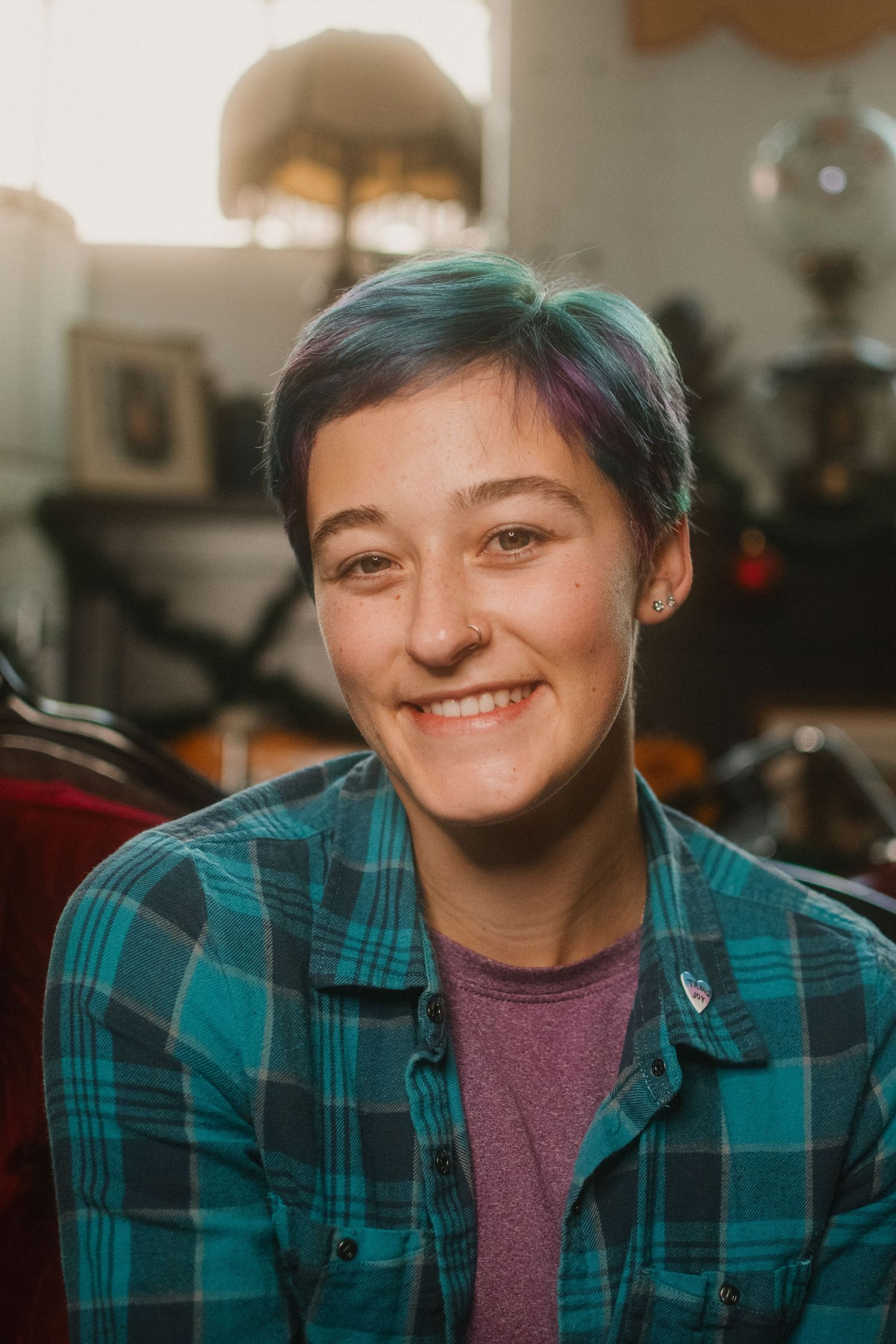 A person wearing a teal plaid flannel shirt and purple t-shirt in a cozy indoor setting.