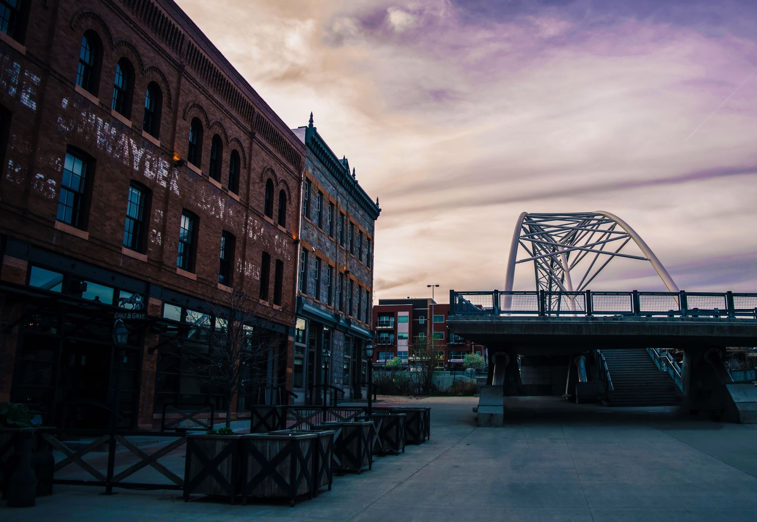 Historic brick buildings and metal bridge structure at dusk with purple sky.