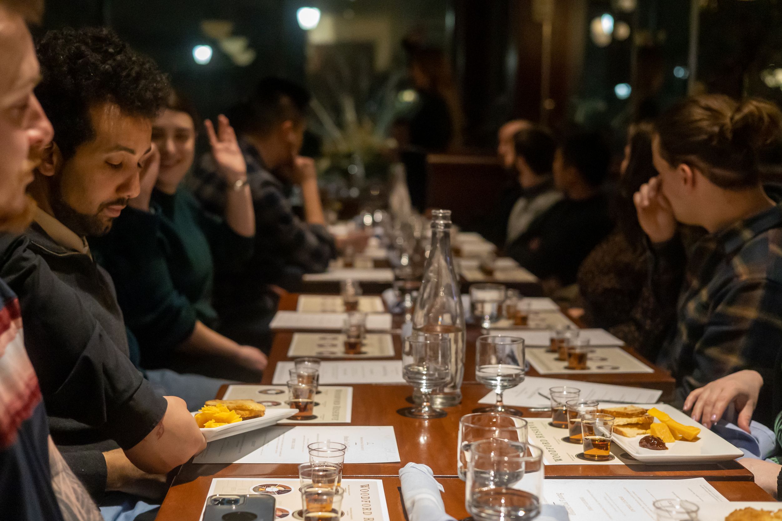 Diners seated at a long table in a dimly lit restaurant enjoying an upscale dining experience.