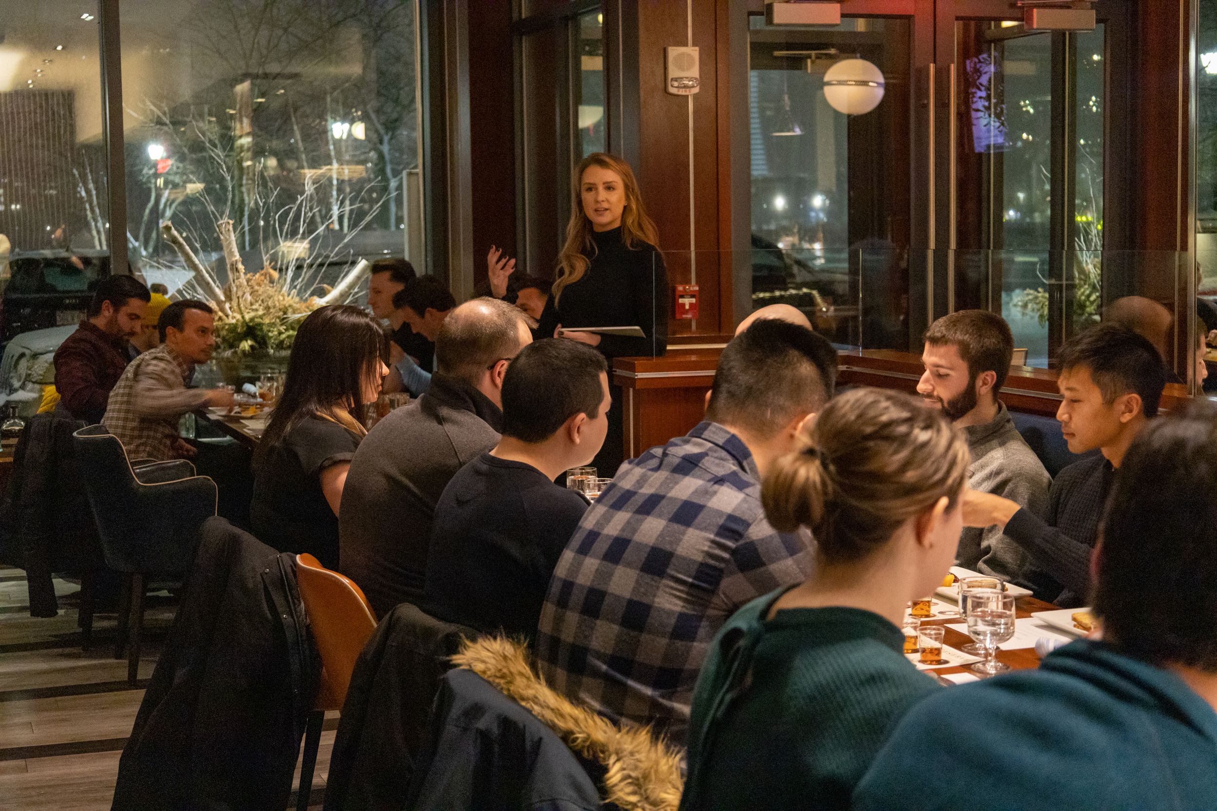 Restaurant patrons gathered around tables for an evening dining event with warm ambient lighting.