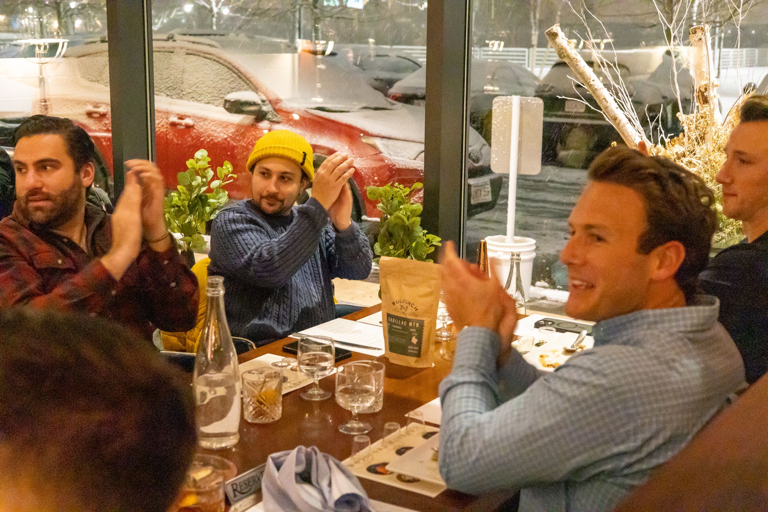 Animated dinner guests enjoying conversation and drinks at a restaurant table.