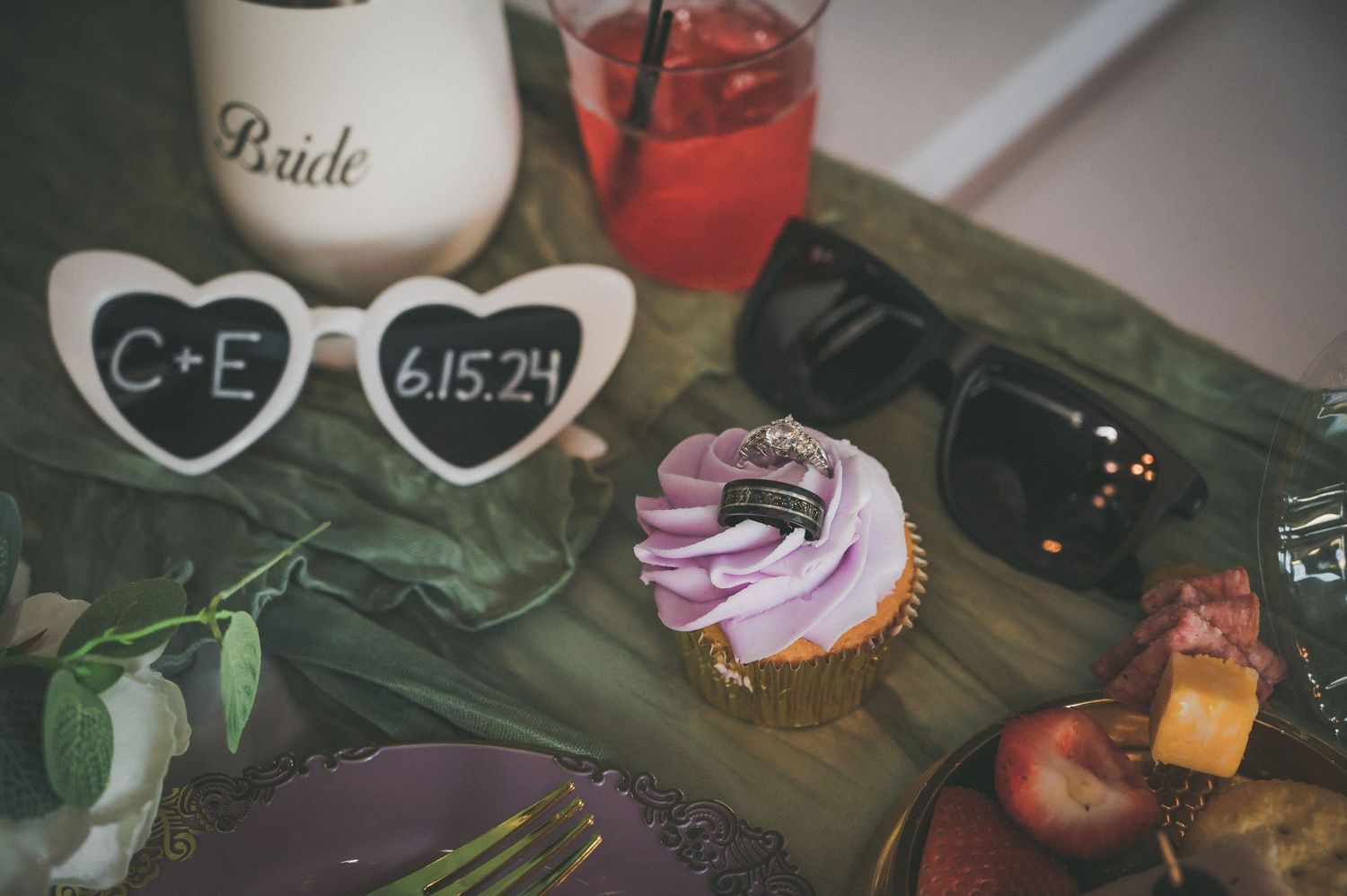 Wedding details with heart-shaped sunglasses, cupcake, and bride inscription on a rustic surface.