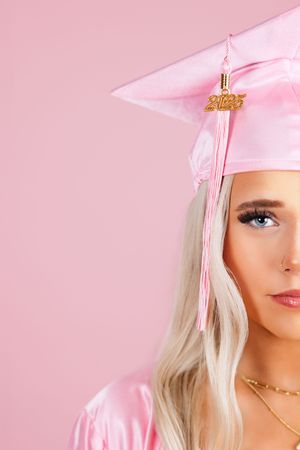 Graduate wearing pink cap and gown with blonde hair against pink background.
