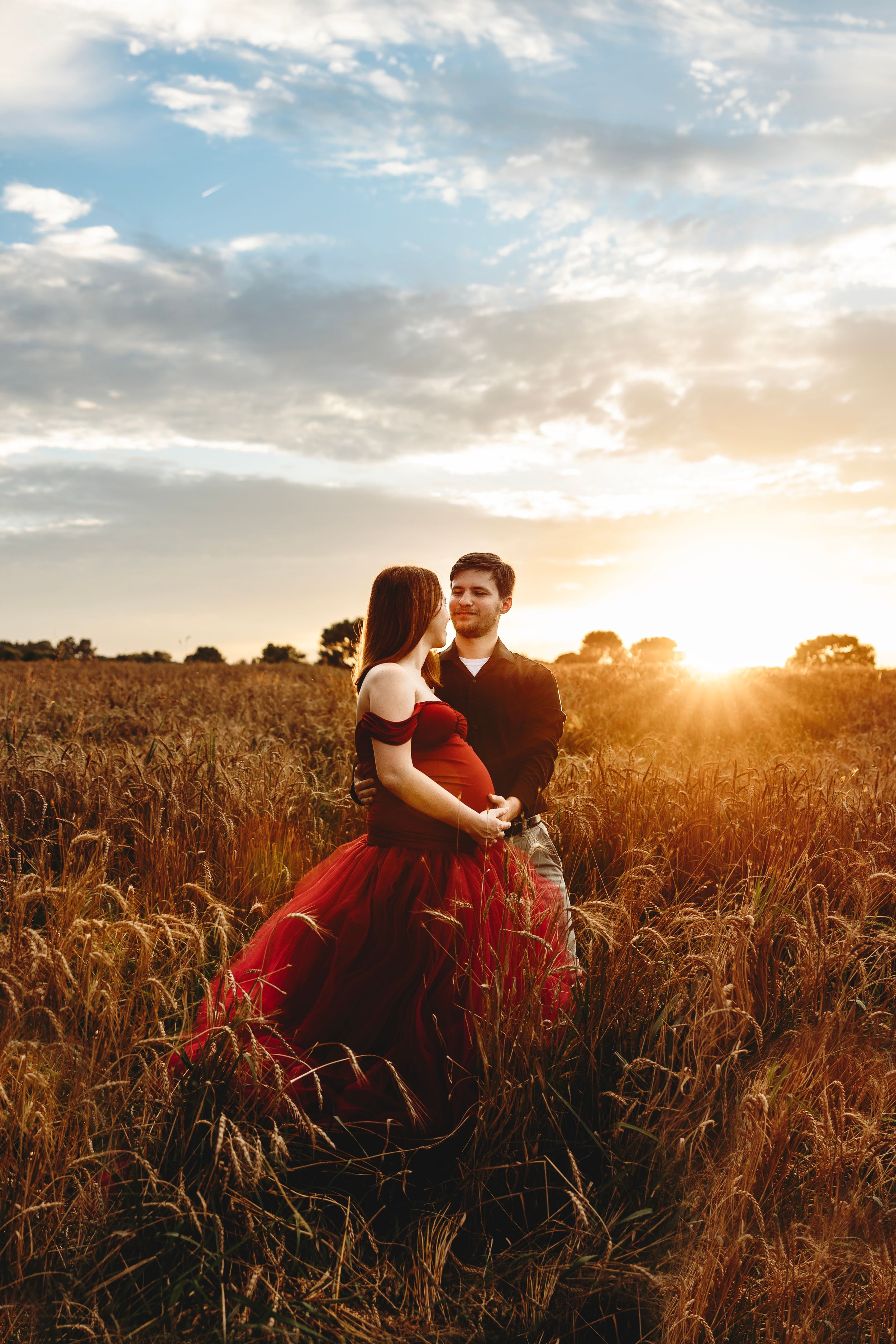 Romantic couple embraces in golden wheat field at sunset creating silhouette against warm sky. Middle TN maternity Photographer.