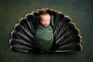 A sleeping baby nestled in a dark green blanket arranged in a fan or peacock tail pattern.