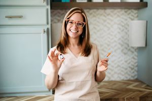Woman in white top sits at desk with laptop and smiles while working from home office with chevron wallpaper.