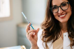 Professional wearing glasses holds up an electronic toothbrush while smiling in a bright indoor setting.