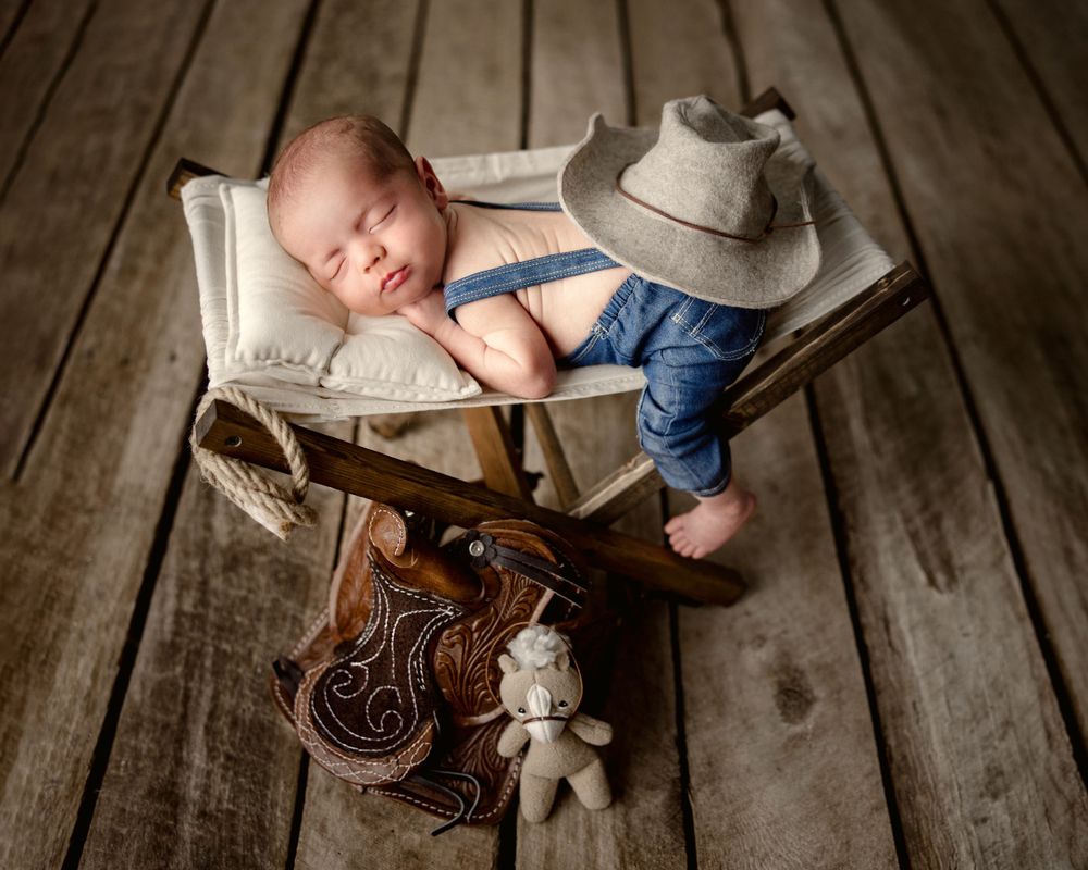 Newborn baby sleeping on wooden floor with cowboy boots and rustic props. Middle TN newborn photographer.