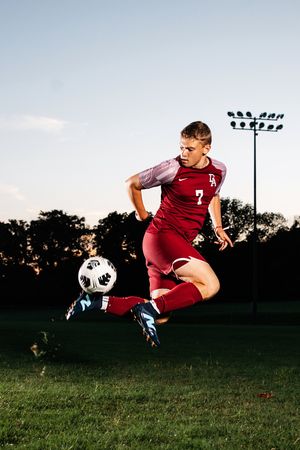 A soccer player performs a dynamic diving header move during a sunset practice session on a grass field.