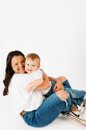A parent and baby share joyful moments while laying on a white studio floor wearing denim and white outfits.