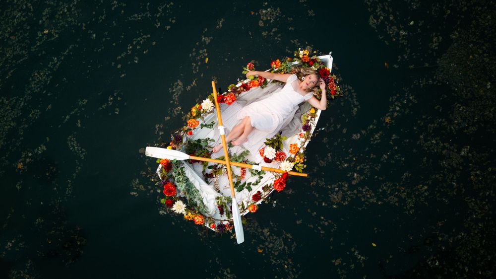 Drone shot of senior in flower covered rowboat in lake.  Middle TN senior photographer.