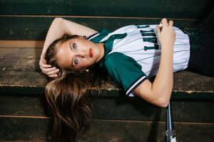 A person in a green and white sports jersey lying on wooden bleachers.