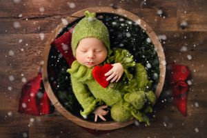 Holiday themed newborn photography with wooden backdrop, snow effects, and festive red and green decorations.