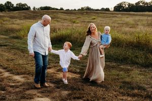 Family members walk together through a golden grassy field during sunset, holding hands and sharing tender moments.