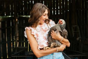A person in a floral dress holds and plays with a small gray dog in a backyard setting.