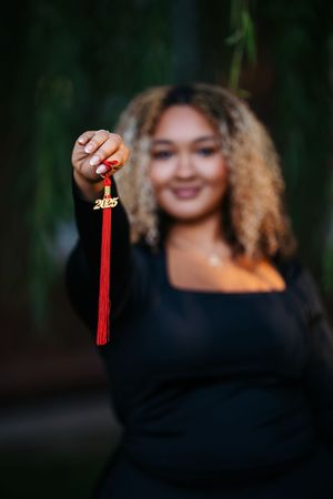 Person in black sweater holds red graduation tassel against dark background in series of photos.