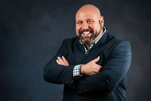 Professional business headshot portrait of someone in a dark suit against a black background with warm lighting.