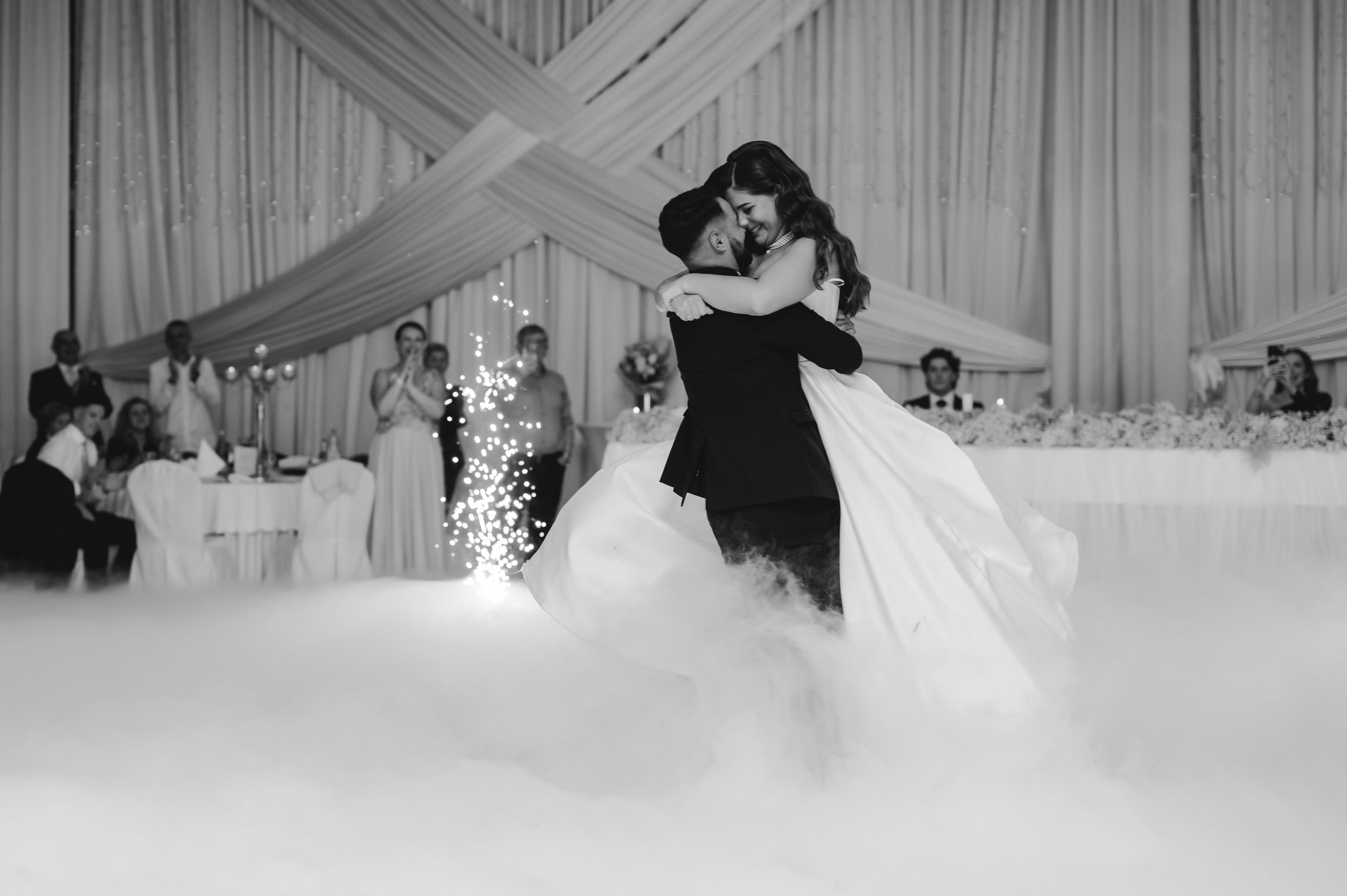 Wedding reception scene in black and white with draped fabric decor and dancing couples.