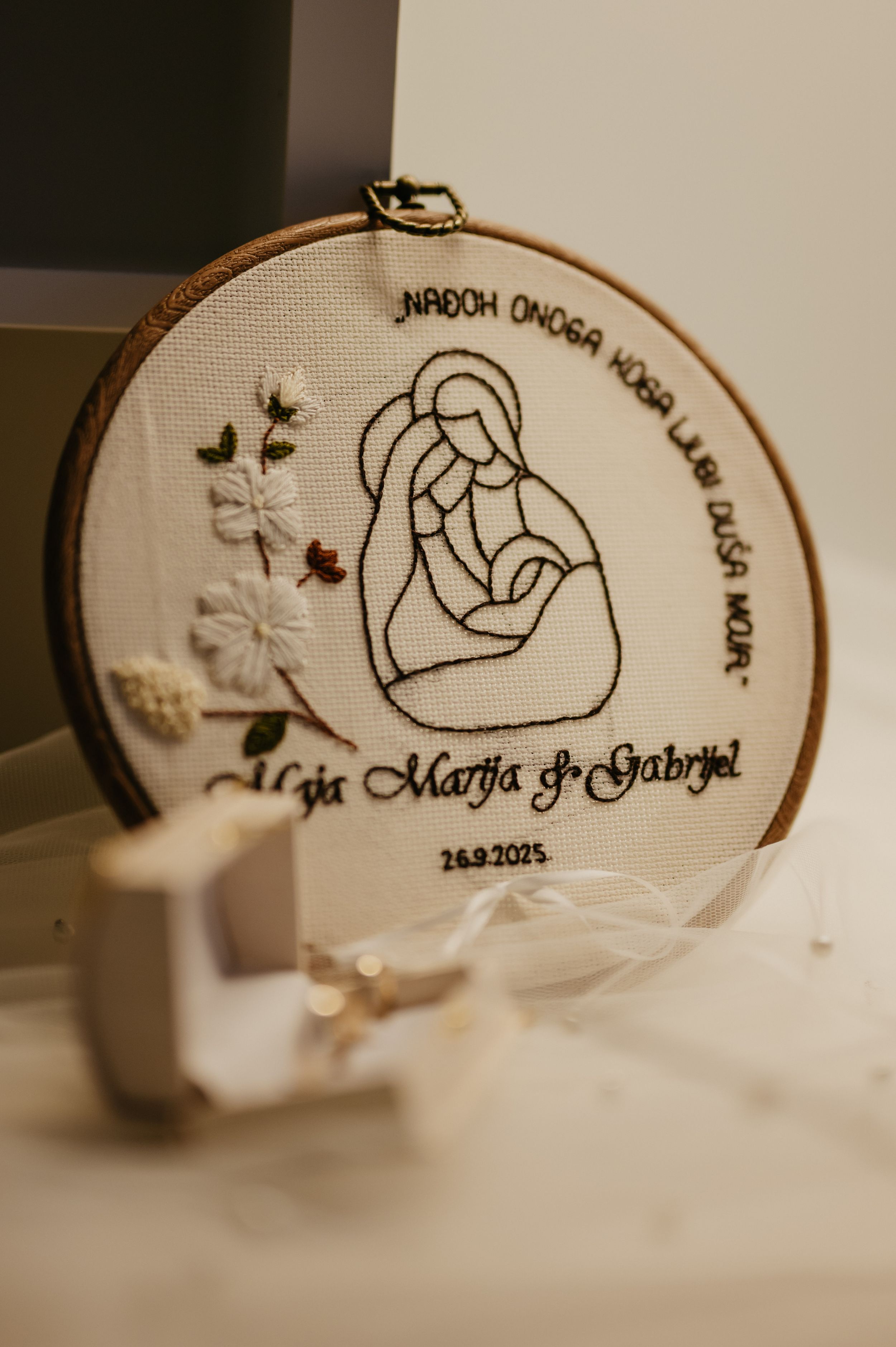 An embroidery hoop displays a minimalist line drawing of mother and child with text and floral details in white fabric.