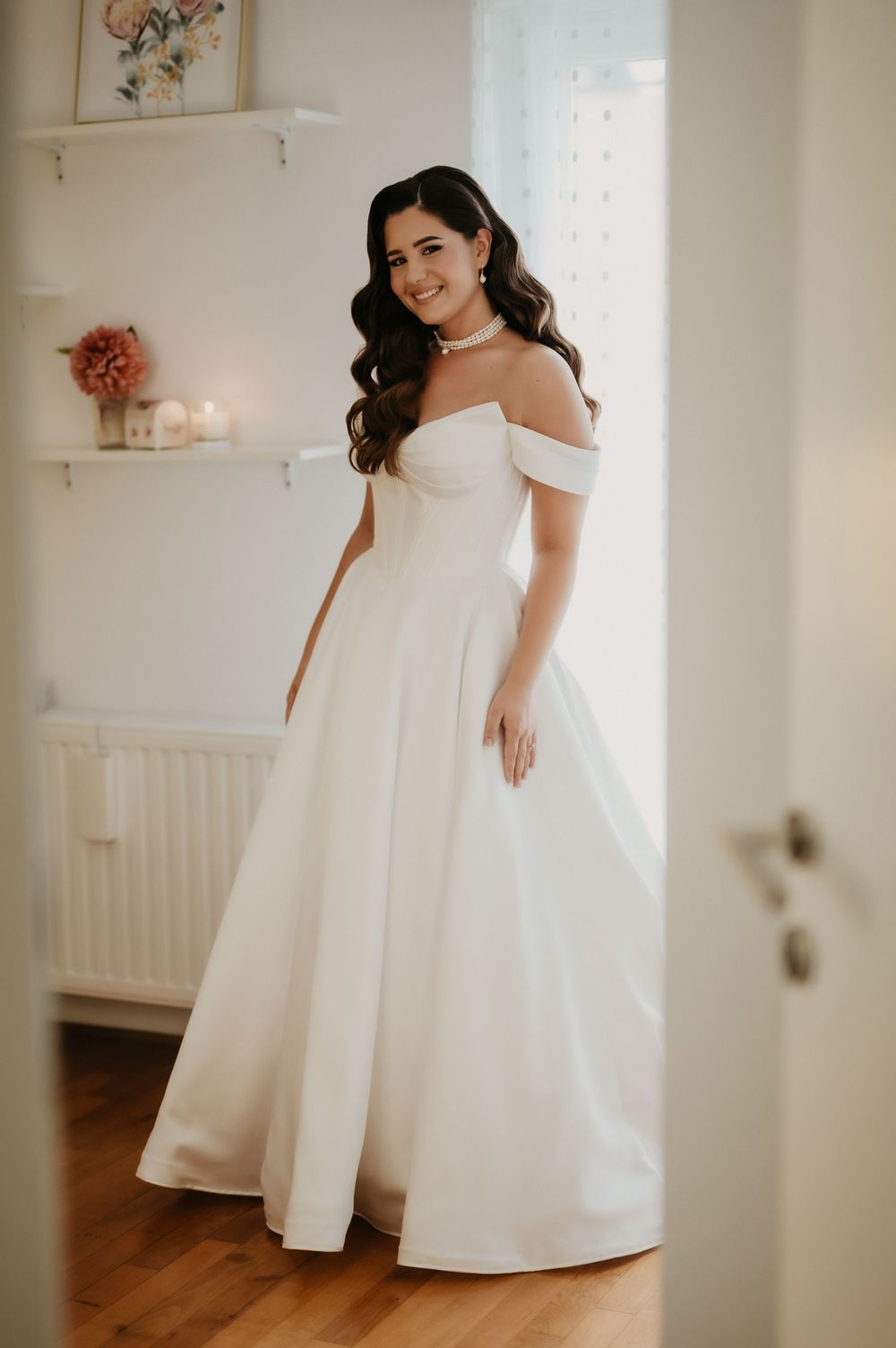 Elegant white wedding dress with off-shoulder design shown in a bright interior setting with soft decor details.