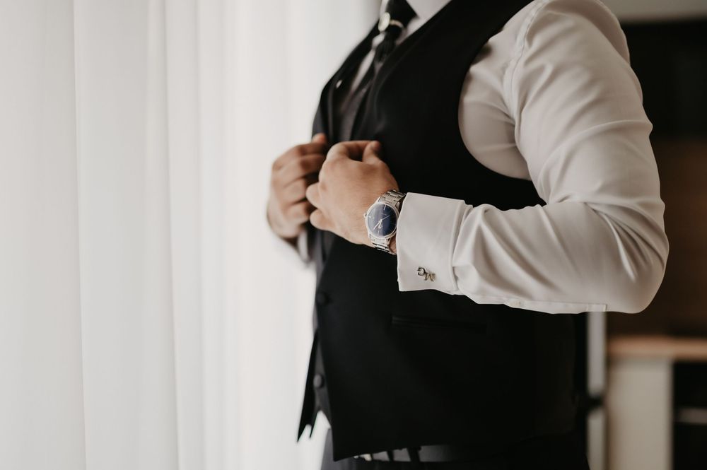 Professional wearing a white button-down shirt and black vest stands confidently with arms crossed in an office setting.