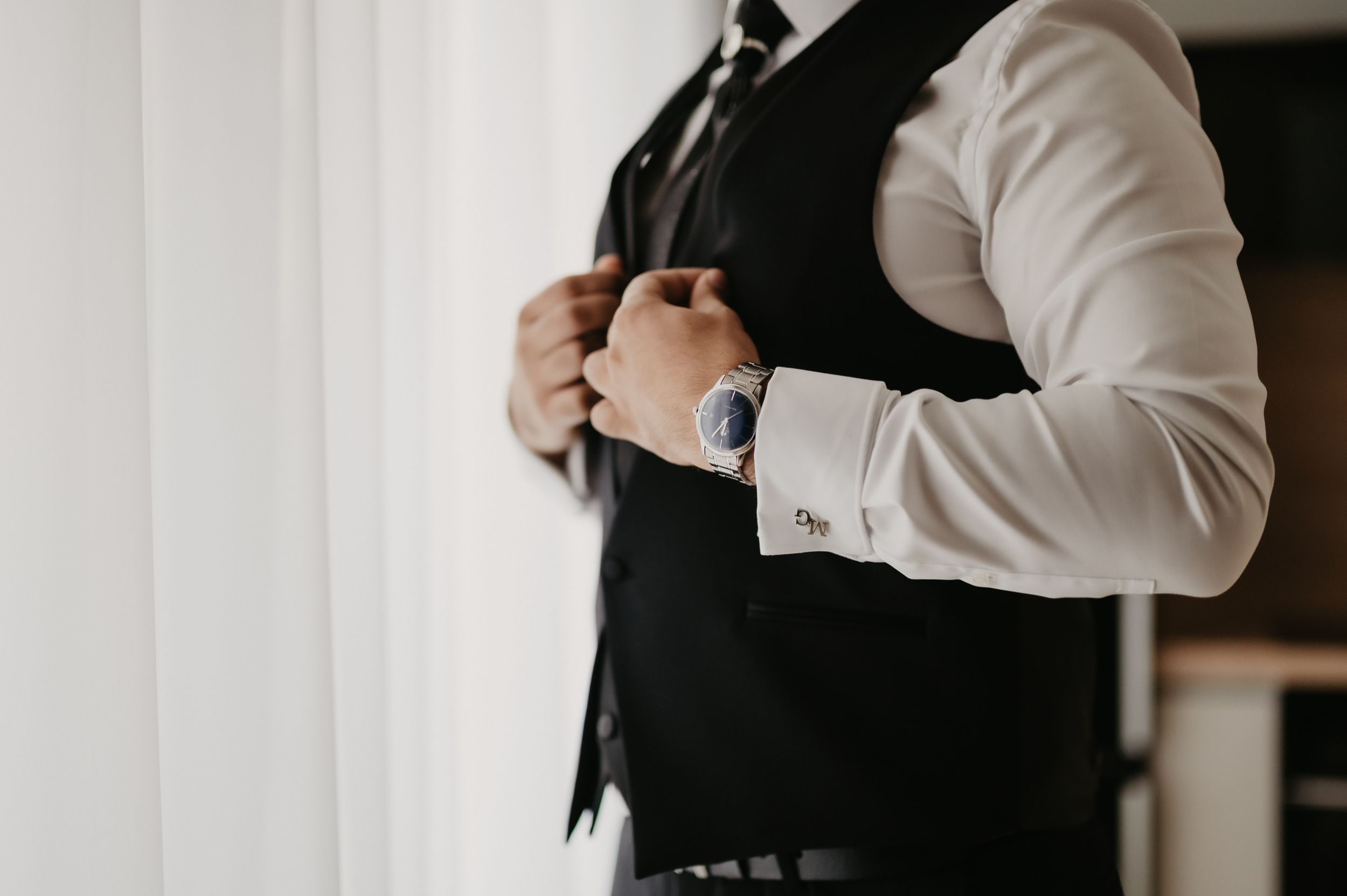 Professional wearing a white button-down shirt and black vest stands confidently with arms crossed in an office setting.