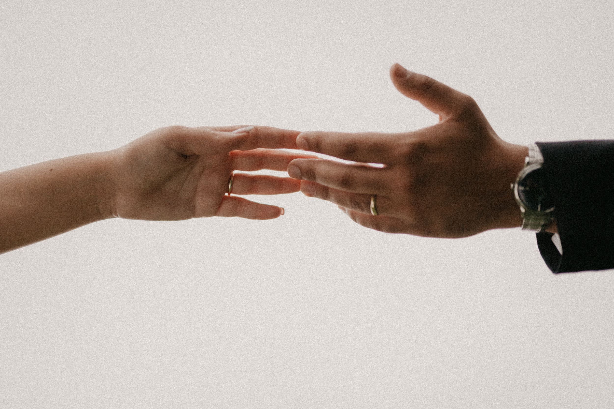 Two hands reaching towards each other against a neutral background in a minimalist composition.