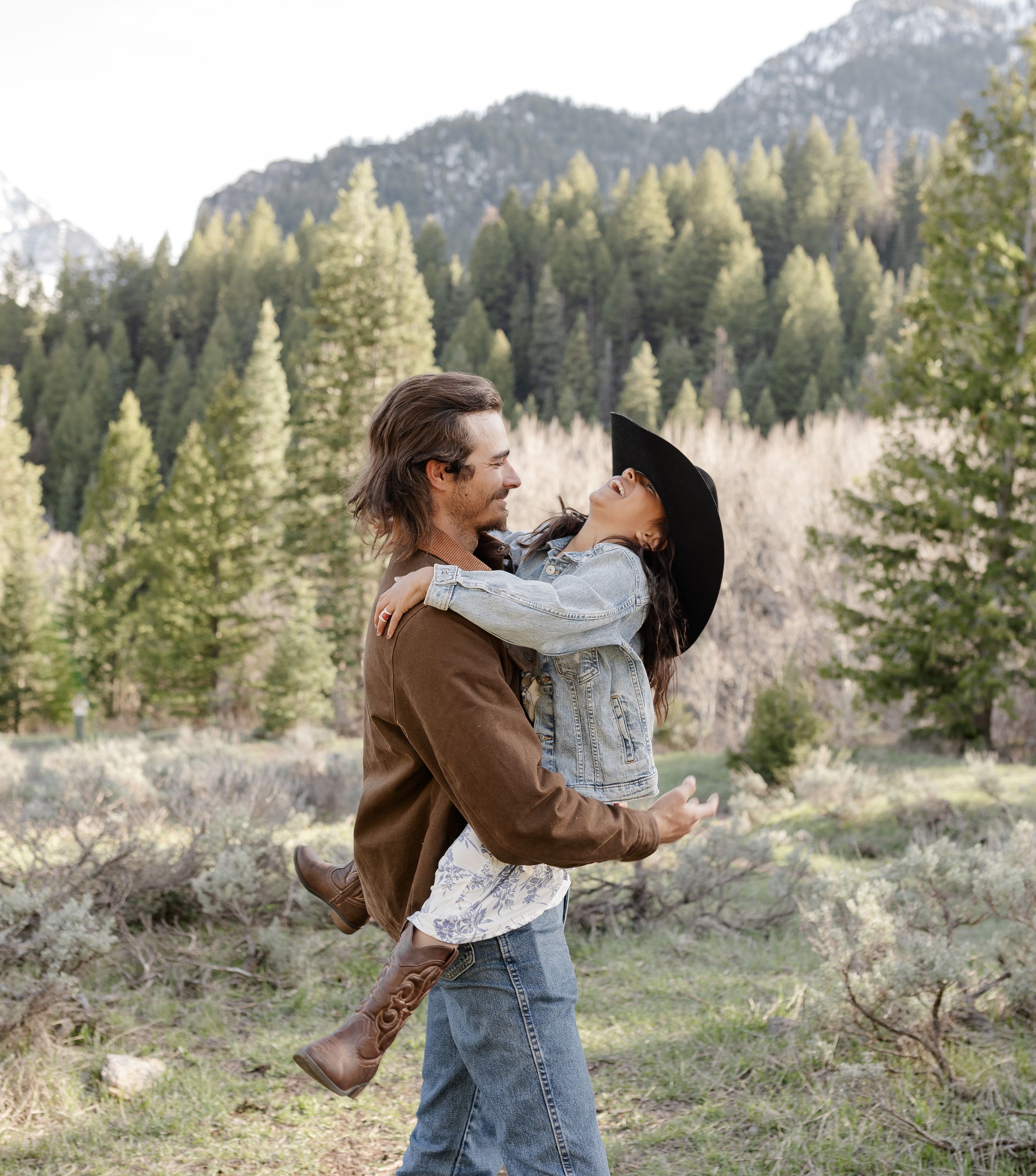 A romantic embrace captured in a scenic mountain landscape with pine trees.