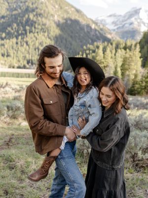 A joyful family moment captured against a backdrop of snow-capped mountains and evergreen trees.