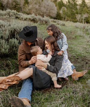 A family in western attire sits together on a grassy hillside sharing an intimate moment outdoors.