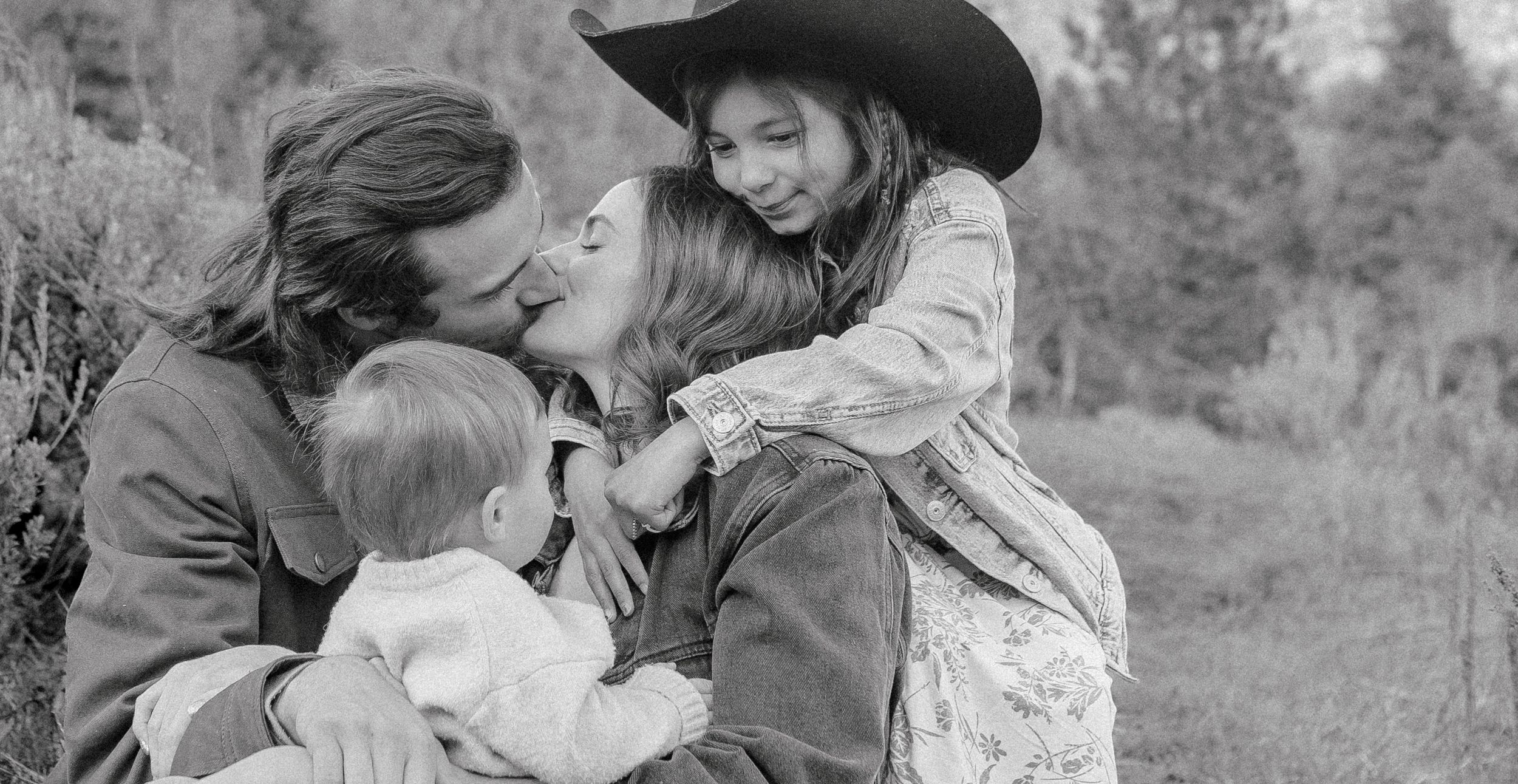 Black and white portrait of a family embracing on a hillside with rustic western styling.
