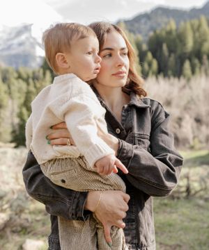 A tender moment between parent and child with mountains and forest in the background.