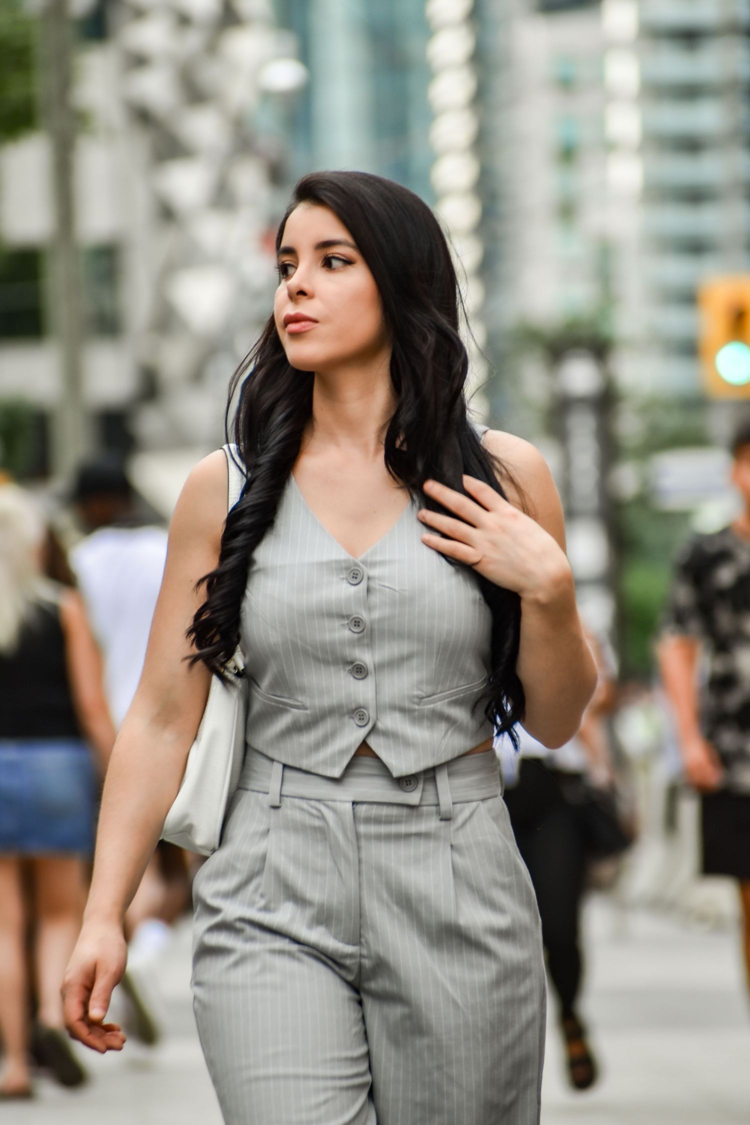 Young woman in grey pinstripe vest and trousers walks confidently on a busy city sidewalk. Toronto GTA