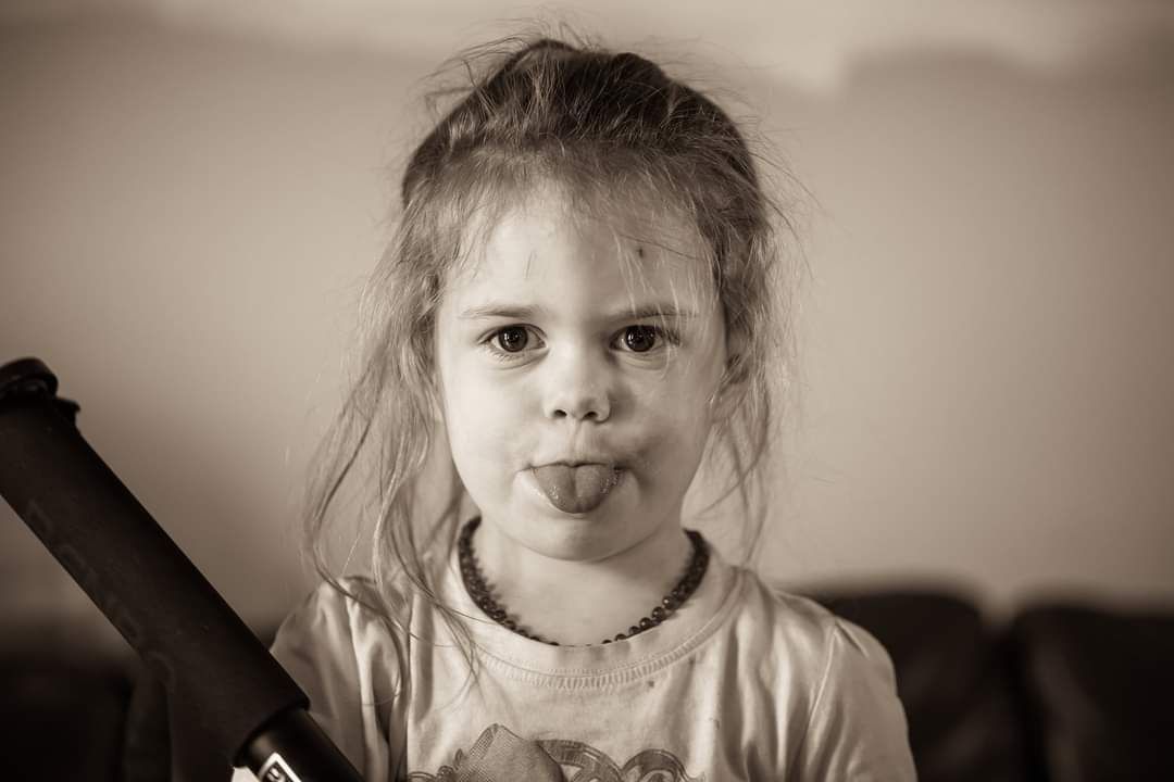 A sepia-toned portrait of a playful child sticking out their tongue.